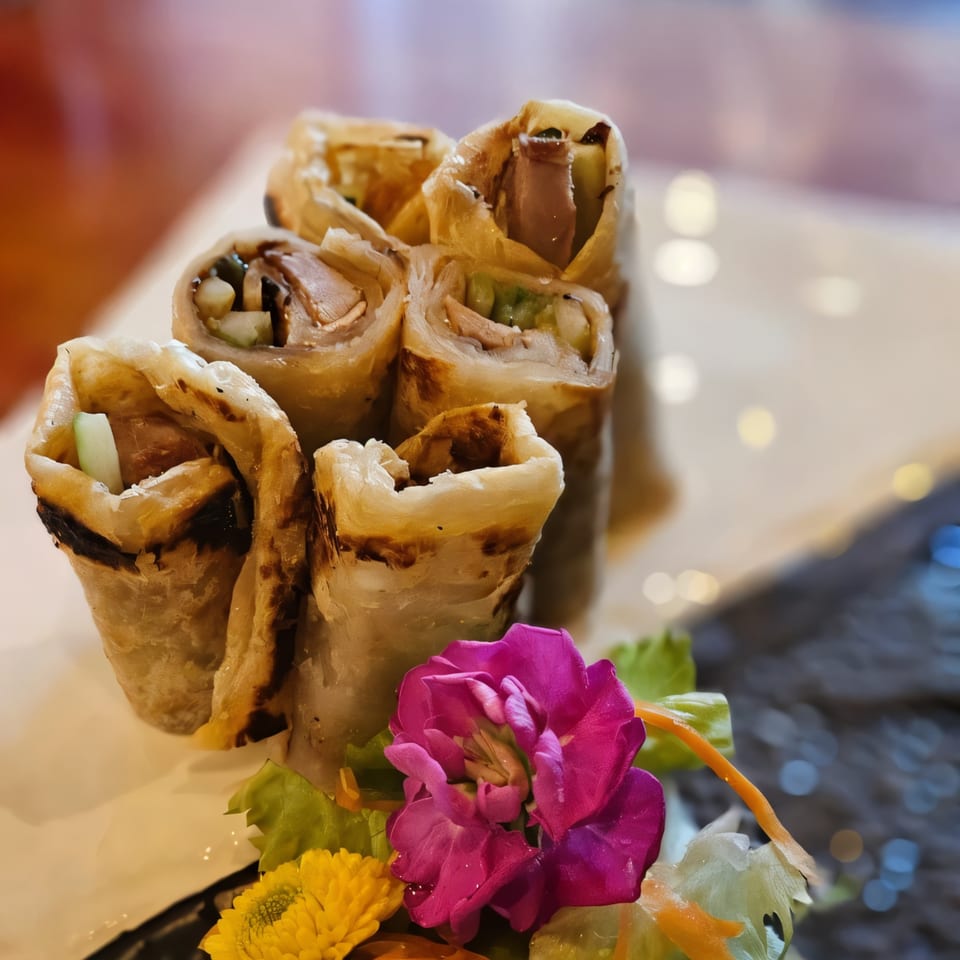 Crispy Thai spring rolls filled with meat and vegetables, garnished with vibrant pink and yellow flowers.