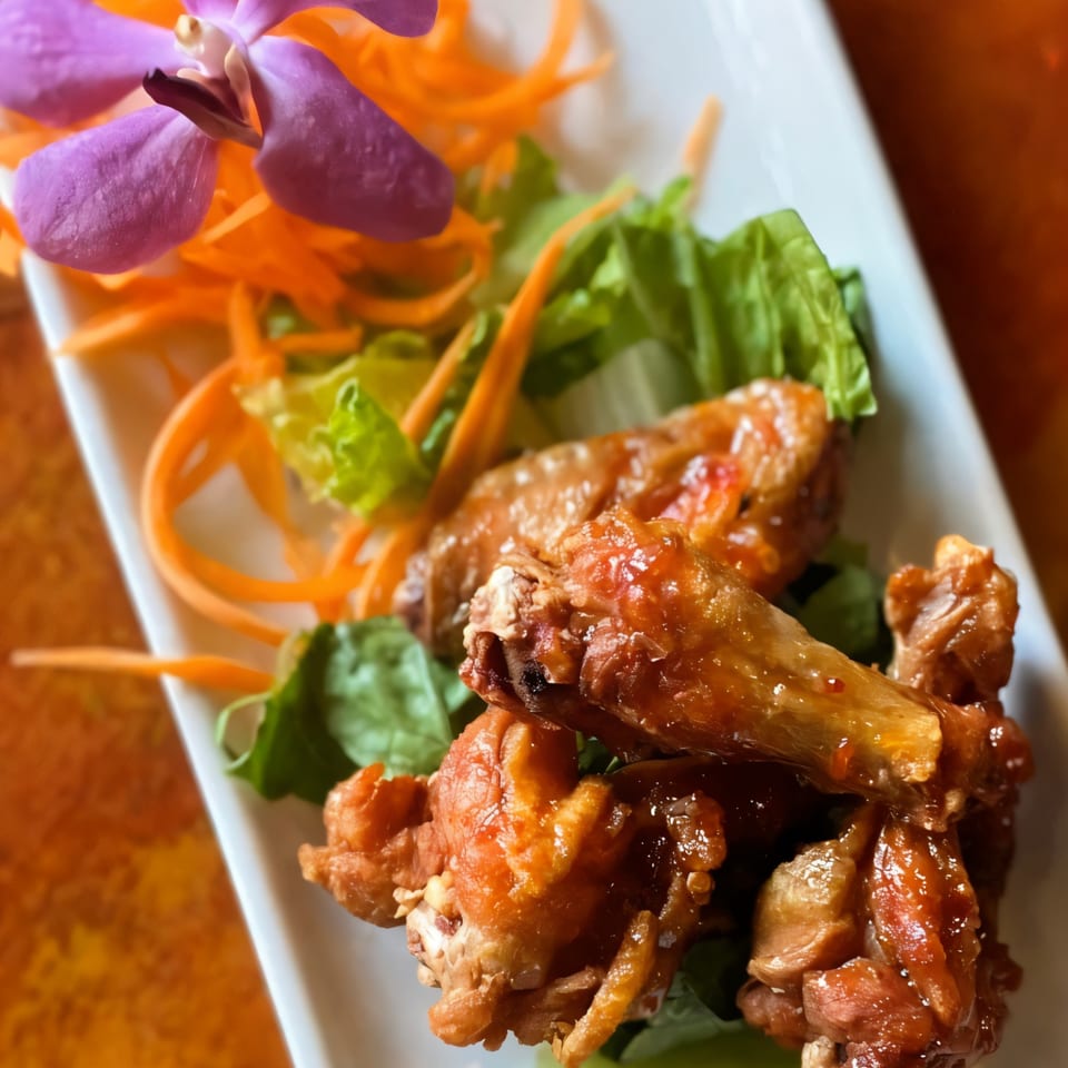 Grata Thai Cuisine's crispy chicken wings with a sweet glaze, garnished with lettuce, carrots, and an orchid.