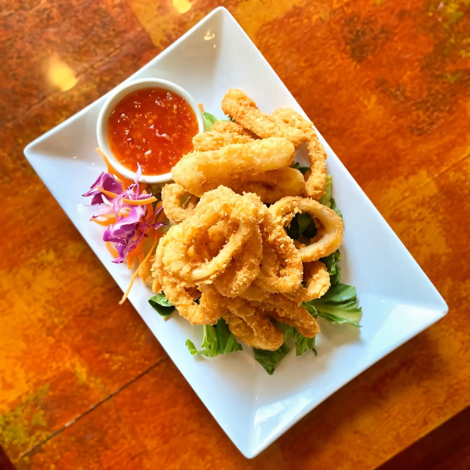 Crispy fried calamari and shrimp on a white plate with sweet chili sauce and shredded vegetables.